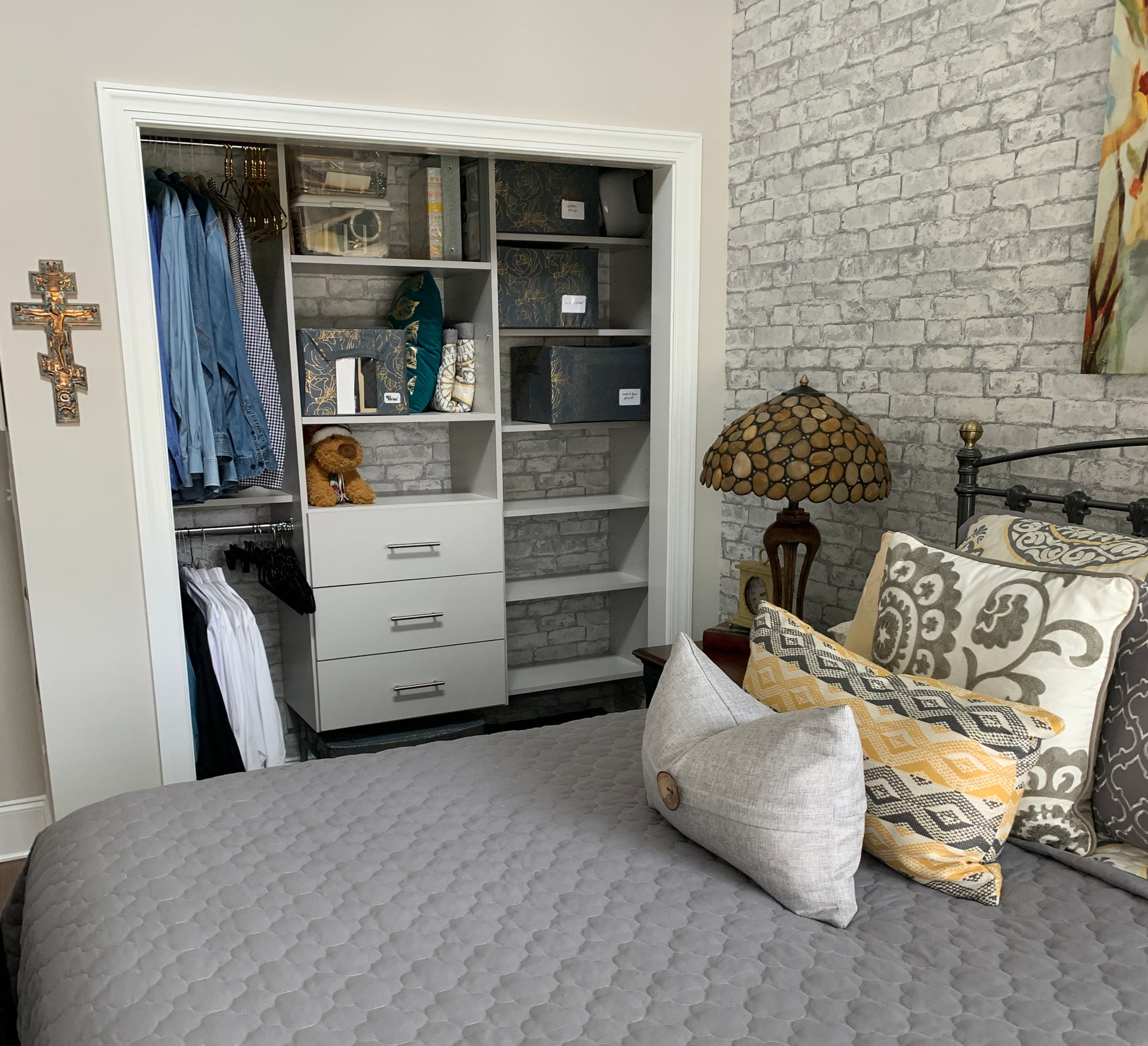 Bedroom with an open closet, neatly organized shelves, and a bed with gray and yellow pillows.