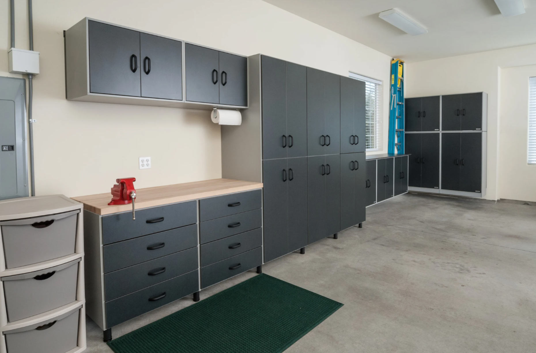 Clean, organized garage with gray cabinets, drawers, a bench, and a small red vise on a wooden countertop.