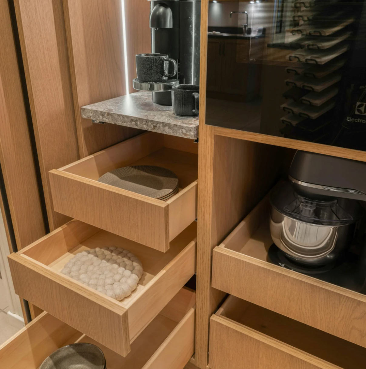 Wooden kitchen cabinets with open drawers, displaying plates and a coffee maker on a pull-out shelf.