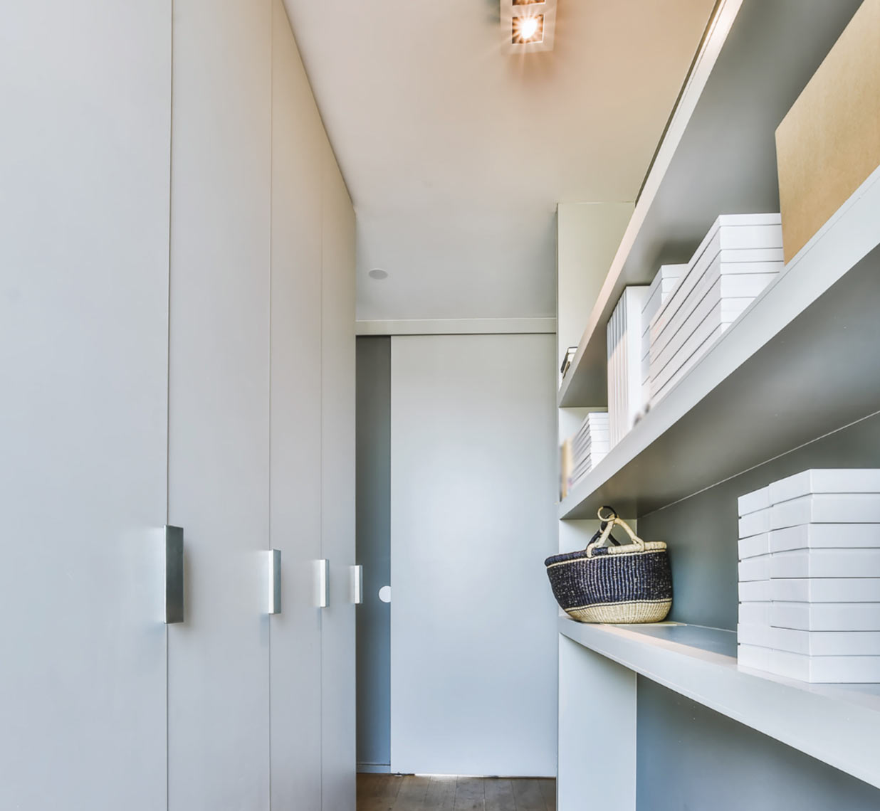 Modern walk-in closet with shelves, stacked white boxes, and a woven basket on a white shelf.