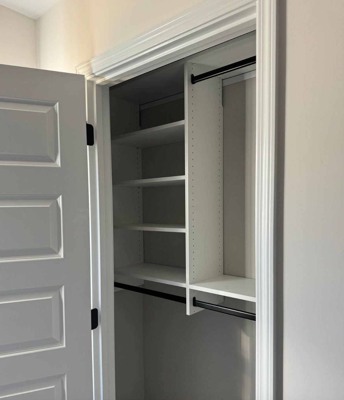 Open door revealing an empty closet with shelves and hanging rods, painted in white and gray tones.