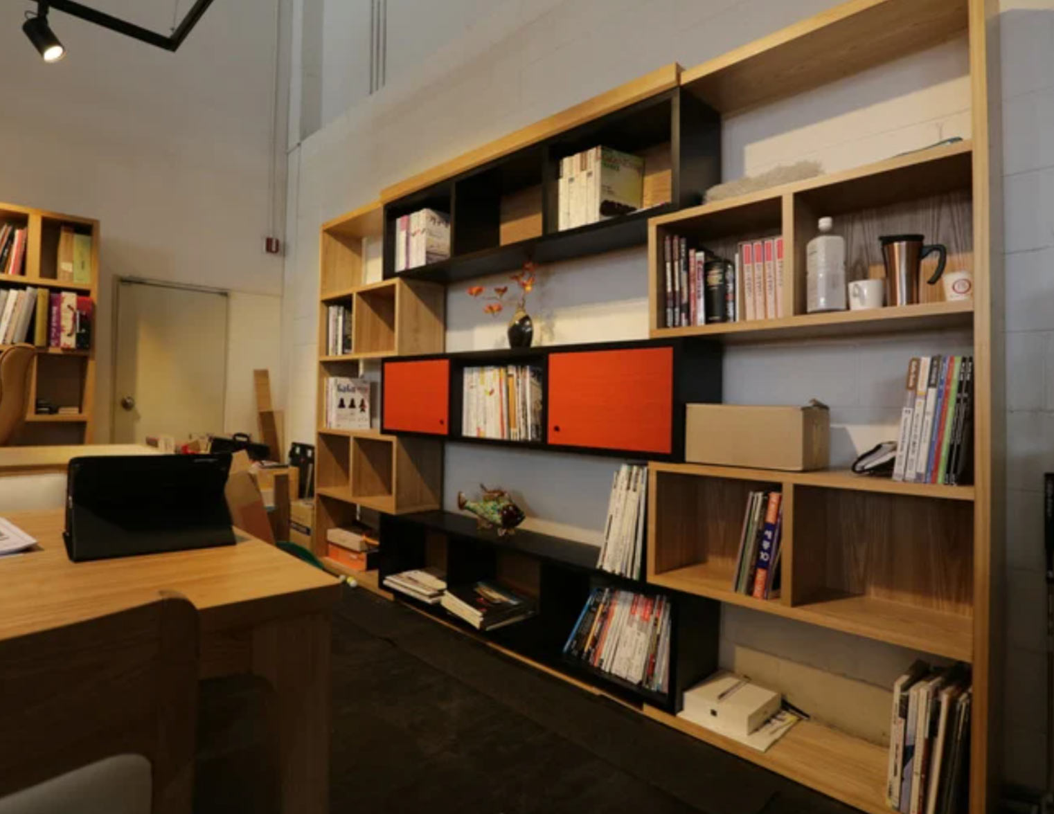 Modern bookshelf with books, boxes, and decor items in a well-lit, organized office space.