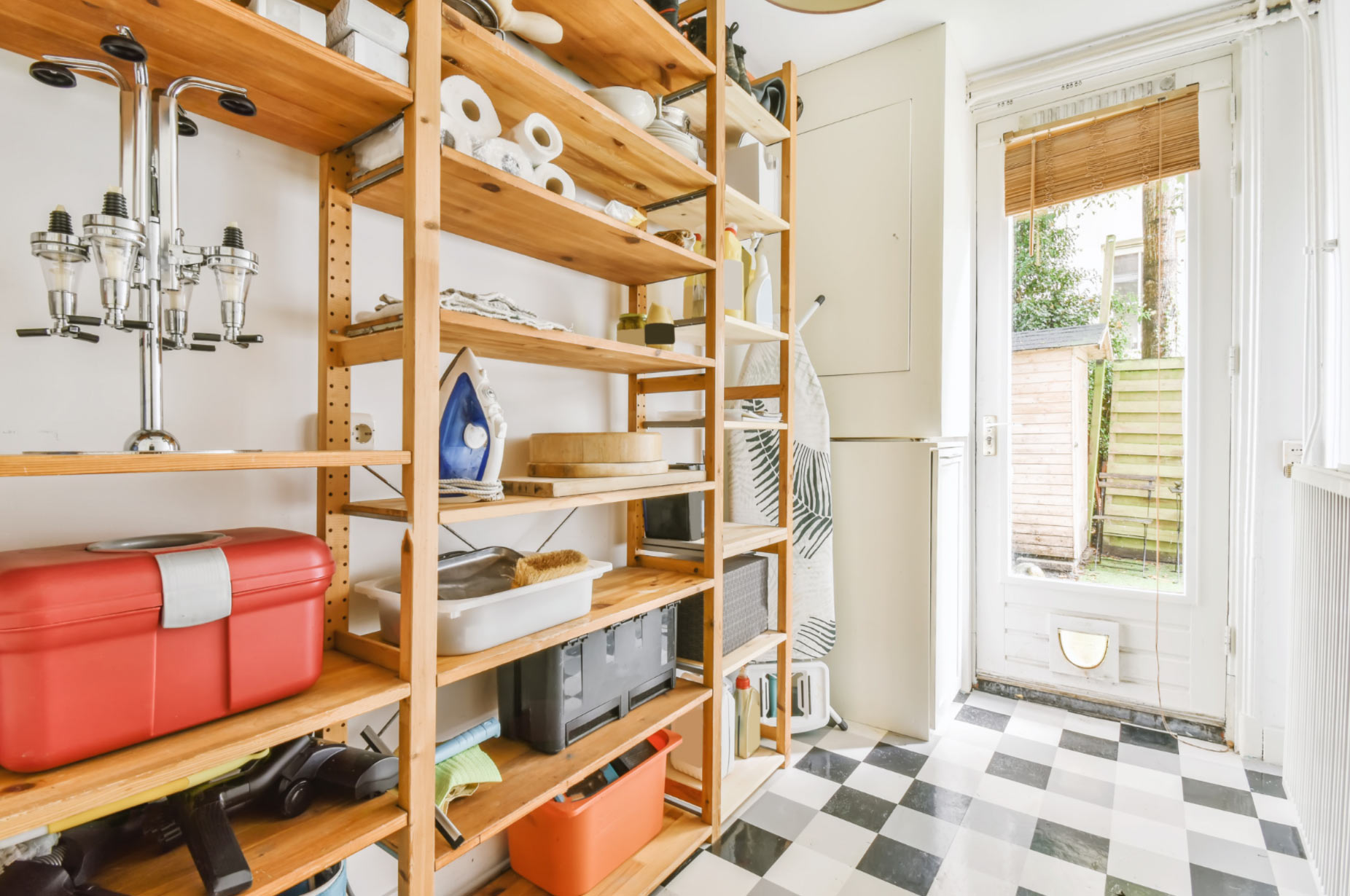 laund-2 Laundry room with wooden shelves, cleaning supplies, an iron, ironing board, and door to outside patio.