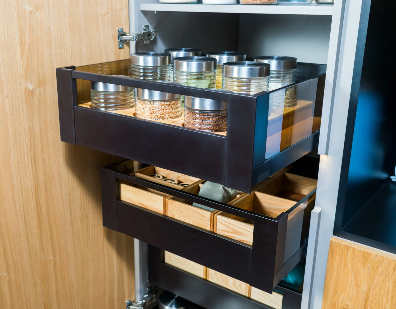 Two pull-out kitchen drawers with jars of dry goods and wooden boxes for storage.